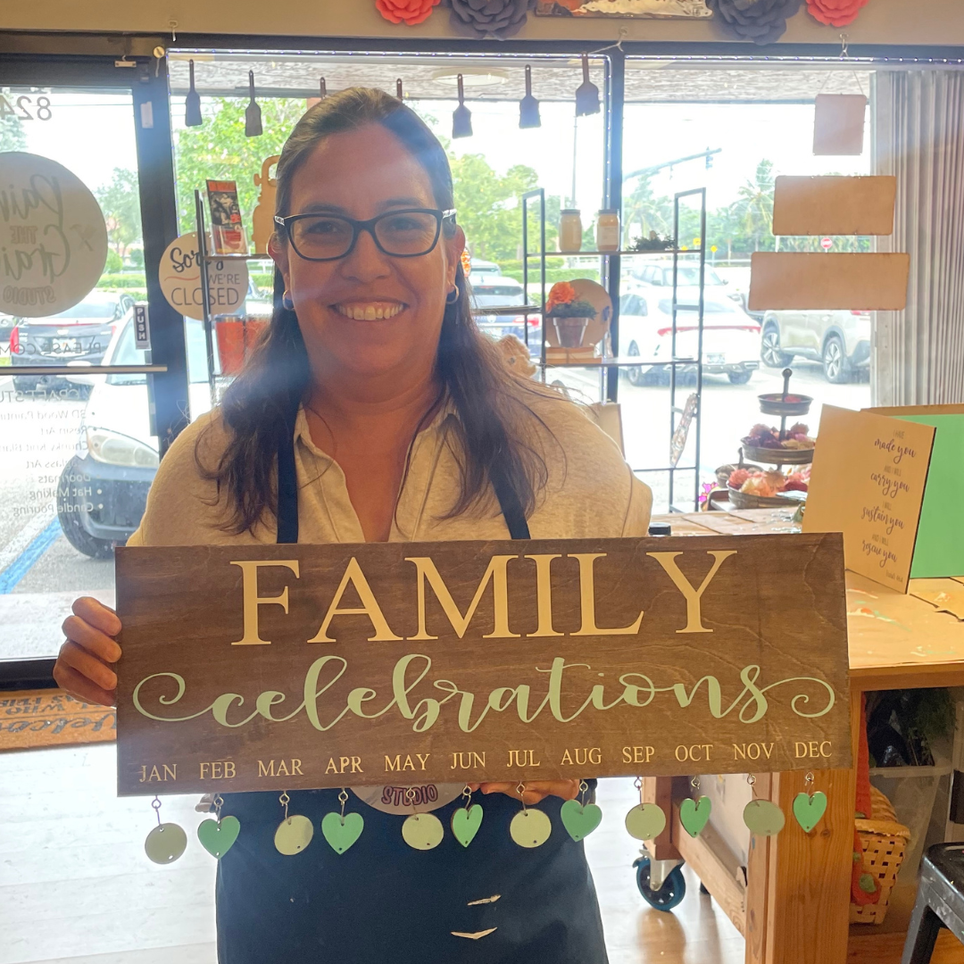 Person holding a wooden sign with 'FAMILY celebrations' text in a store setting.