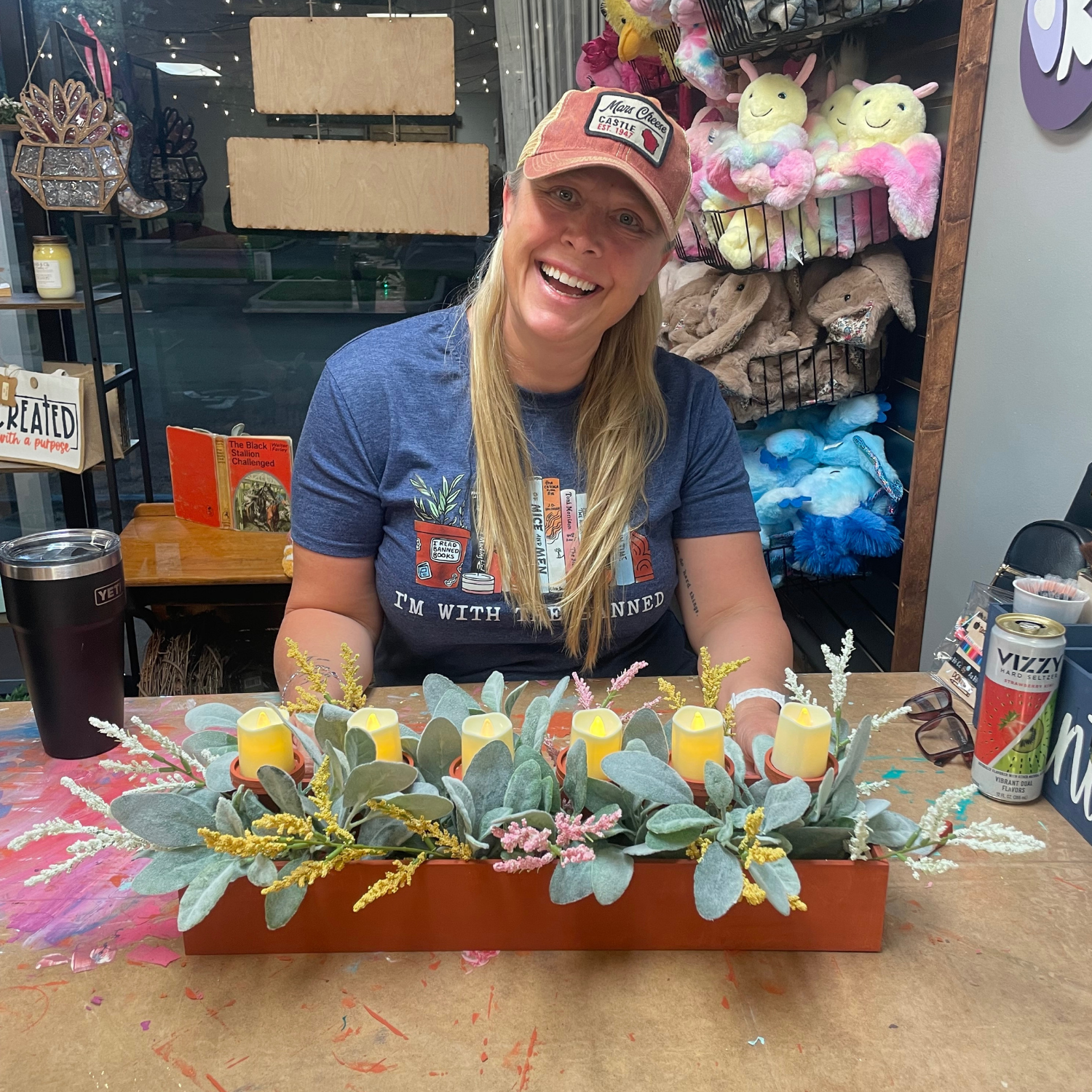 Person sitting at a table with a decorative plant arrangement featuring candles, in a store setting.