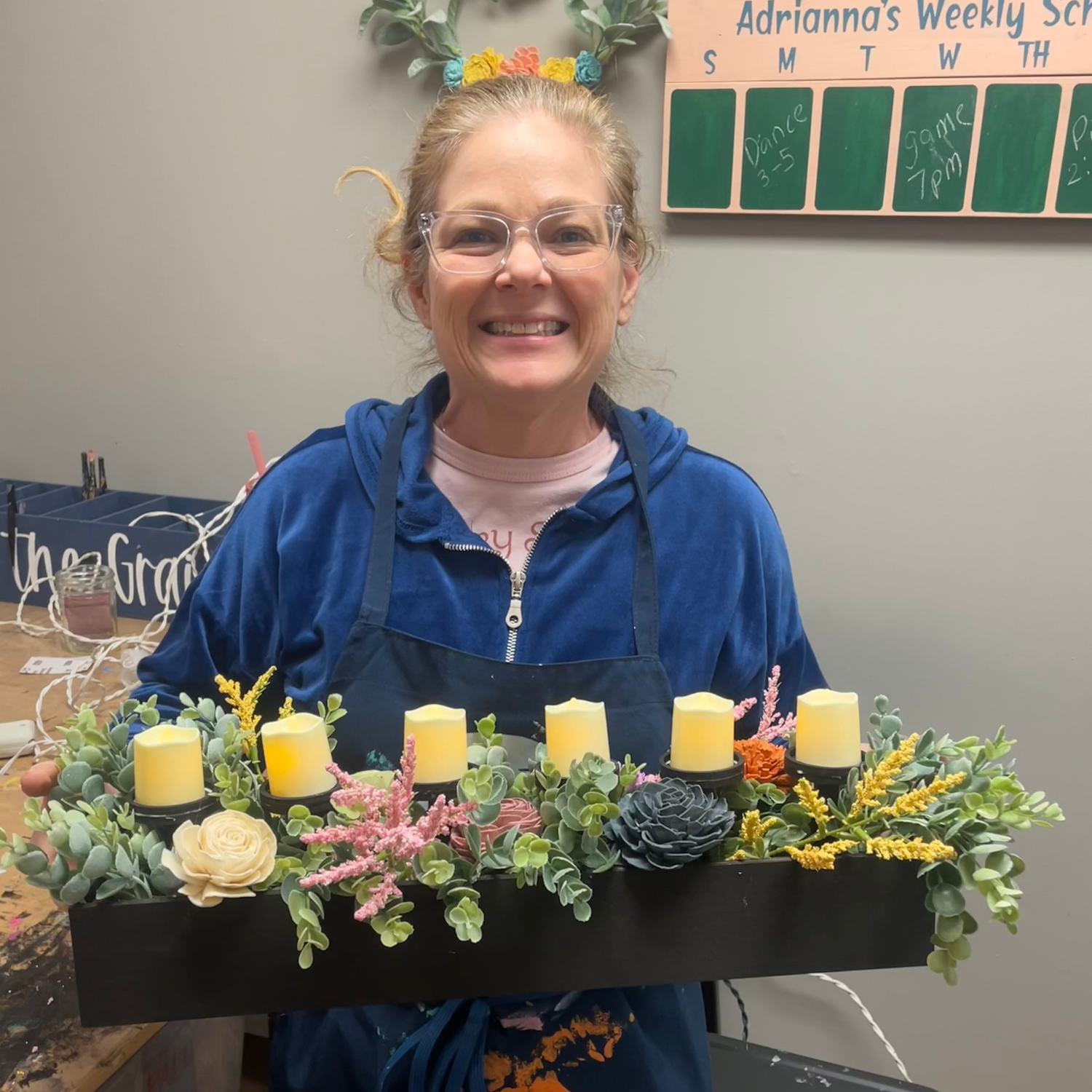 Person holding a decorative centerpiece with candles and flowers in a diy studio setting
